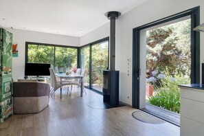 A modern kitchen with a large window, a dining area with a table and chairs, and a built-in wood stove. - Holiday Home 'Aux Jolis Bambous, Garden' with Private Terrace and Garden (Pornic)