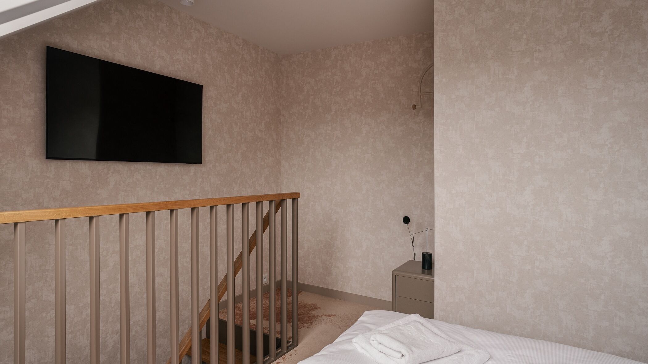 Un dormitorio con una cama, barandilla de madera, mesita de noche y televisor montado en la pared.