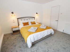 A neatly arranged bedroom with a bed, bedside tables, and a door. - Saltaire House (Shipley)