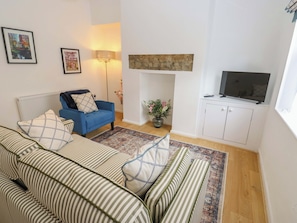 A living room with a sofa set, a blue armchair, a floor lamp, a fireplace, a TV, and a cabinet. - Saltaire House (Shipley)