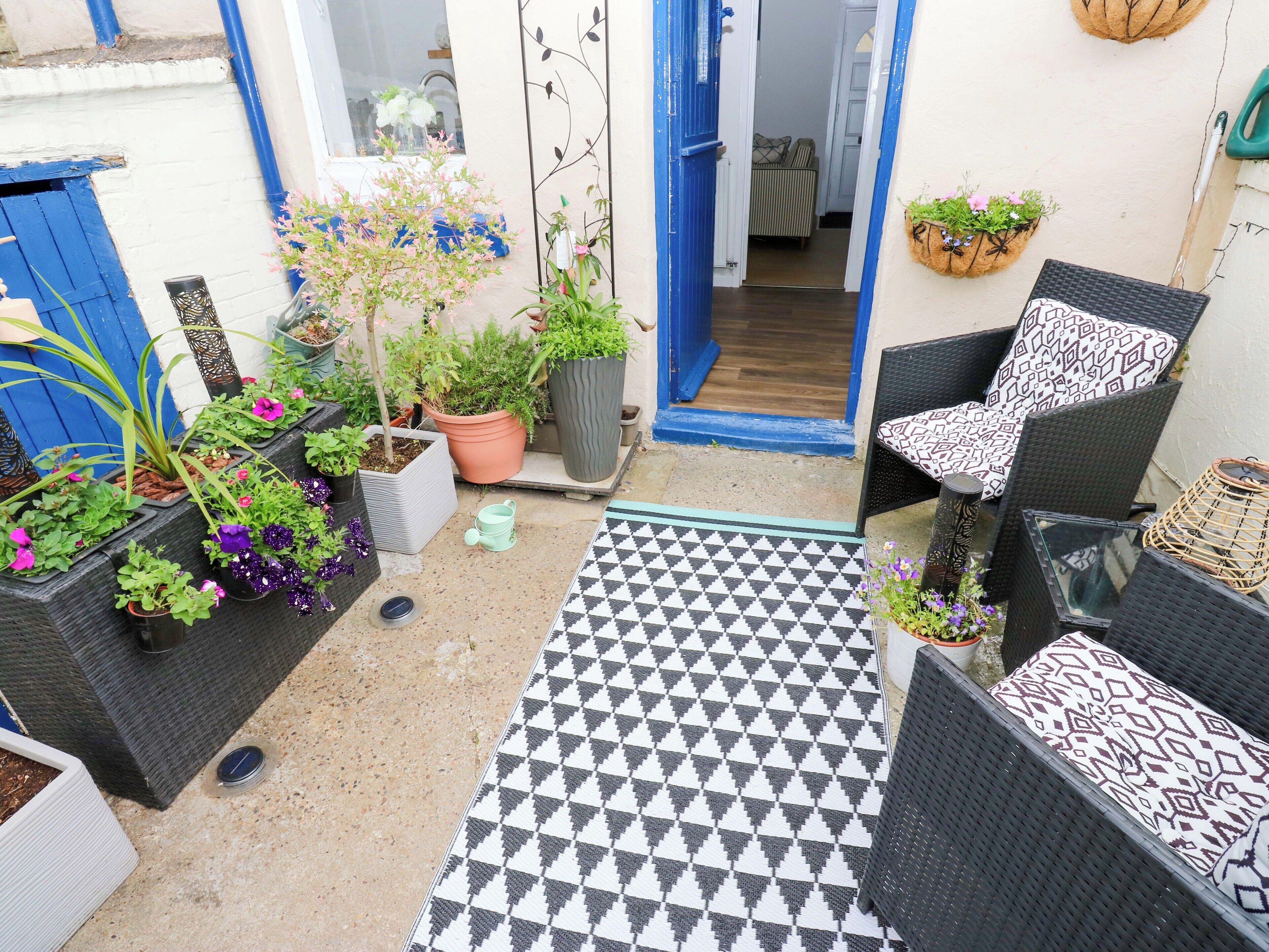 En terrasse med udendørs møbler, plantekrukker og et mønstret tæppe.