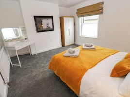 A bedroom with a bed, a desk, a mirror, a wardrobe, and a window with a curtain.