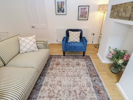 Una habitación con un sofá a rayas, un sillón azul, un tapete estampado y un jarrón con flores.