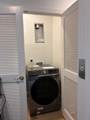 Un cuarto de lavandería con lavadora y secadora Samsung, una ventana pequeña y una puerta con picaporte.