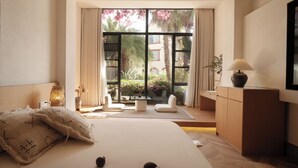A bedroom with a large bed, a desk, a chair, and a view of a garden through a large window.