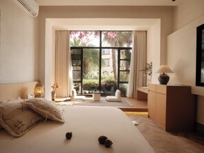 A bedroom with a large bed, a desk, a chair, and a view of a garden through a large window.