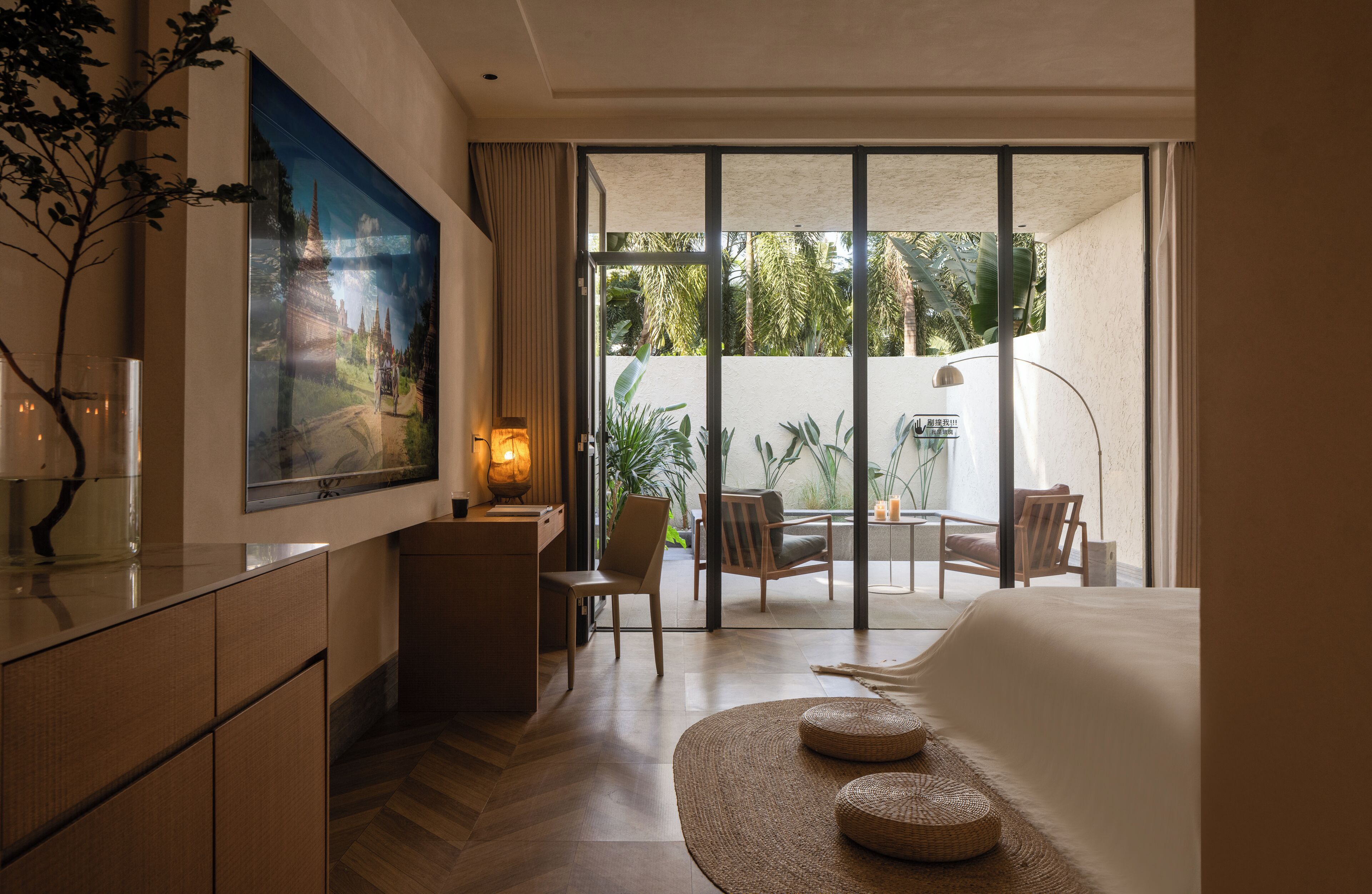 A hotel room with a large window, a desk, a chair, a bed, and a painting on the wall.