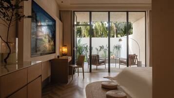 A hotel room with a large window, a desk, a chair, a bed, and a painting on the wall.