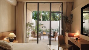 Habitación de hotel con cama, escritorio, sillas, una mesita con velas y vistas a un jardín a través de una puerta corredera.