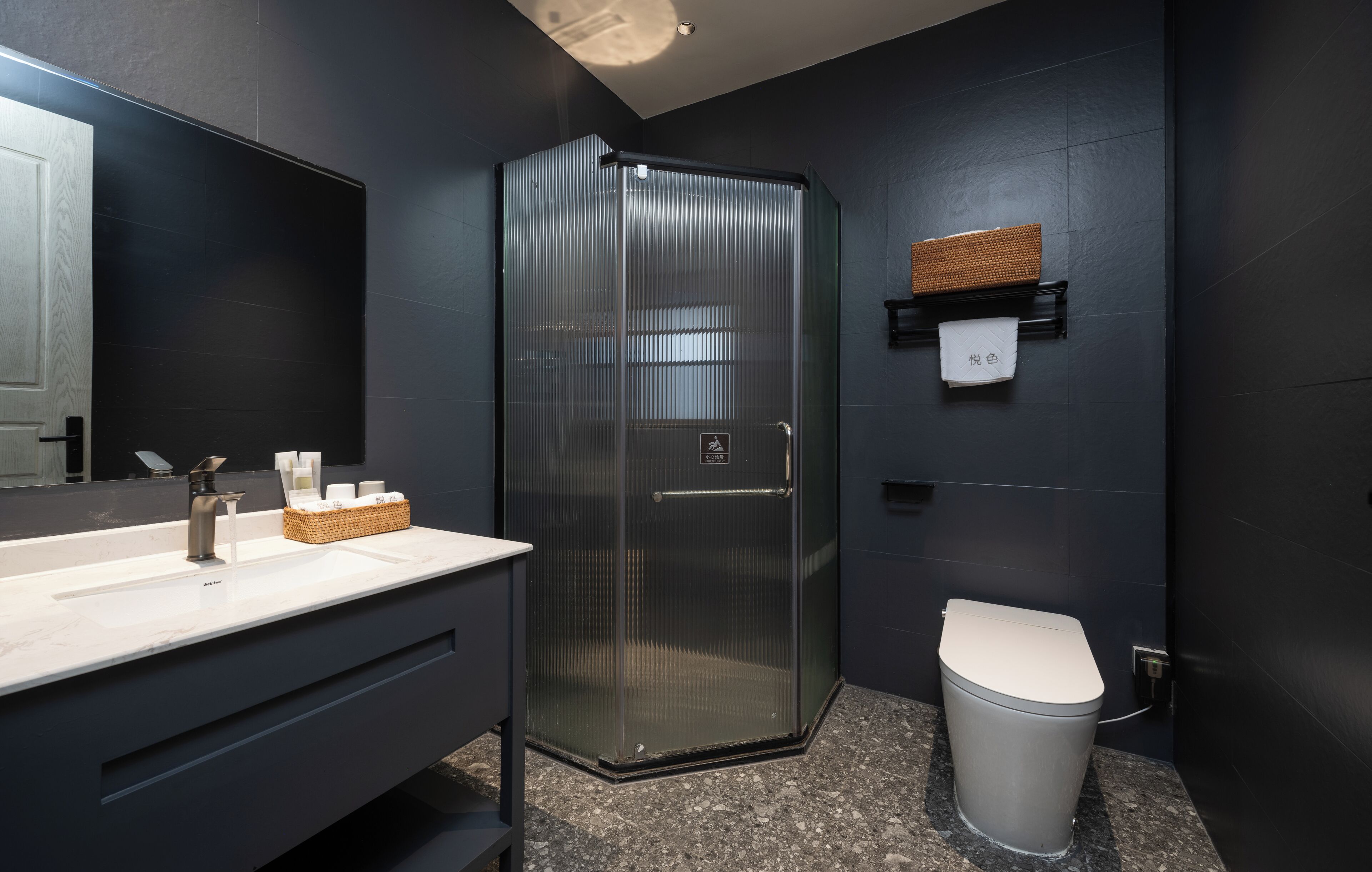 A modern bathroom with a glass shower enclosure, a white sink with marble countertop, and a toilet.