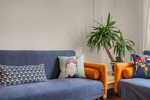 Un saló amb un sofà blau, un coixí amb dibuixos, un coixí de punts i una planta en test.