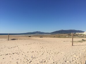En strand med fotspår i sanden, en klar himmel och avlägsna berg.