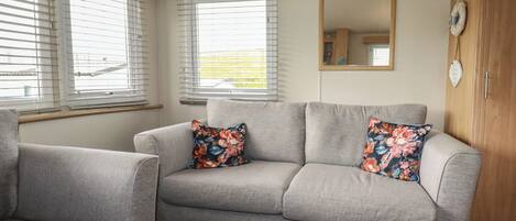 A grey sofa with floral cushions, a wooden cabinet, and a mirror on the wall.