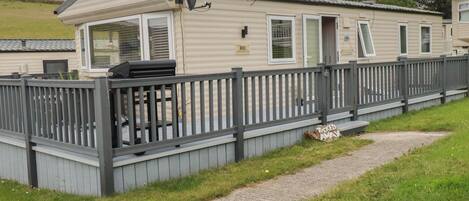 A mobile home with a fenced deck, a grill, and a sign that reads 'Tucked Away'.