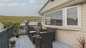 A deck with wicker furniture and potted plants, overlooking a grassy field. - Tucked Away (Newquay)