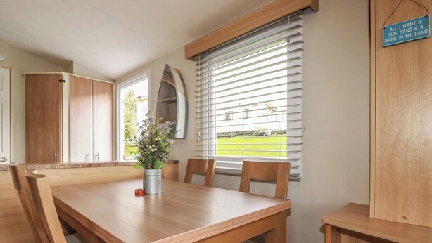 A dining area with a wooden table, chairs, a potted plant, and a window with blinds. - Tucked Away (Newquay)