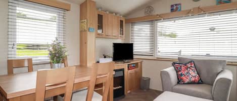 A compact living space with a dining table, chairs, a sofa, a TV, and a small kitchen area.