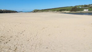A wide sandy beach with a clear sky, distant hills, and a few buildings on the right. - Tucked Away (Newquay)
