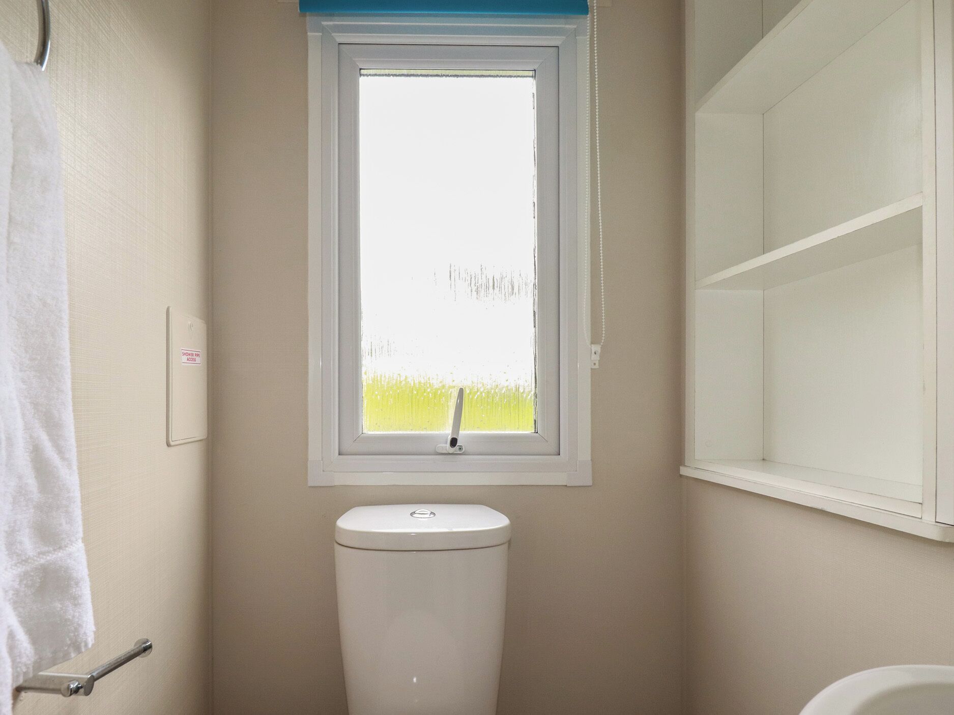 A small bathroom with a toilet, a window, and a towel rack.