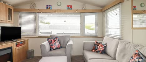 Una sala de estar acogedora con sofá, sillón, otoman, televisor y mueble de madera.