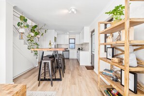A modern kitchen with a central island, bar stools, hanging plants, and a wooden bookshelf. - 42 Kronenbosch at West Beach (Cape Town)