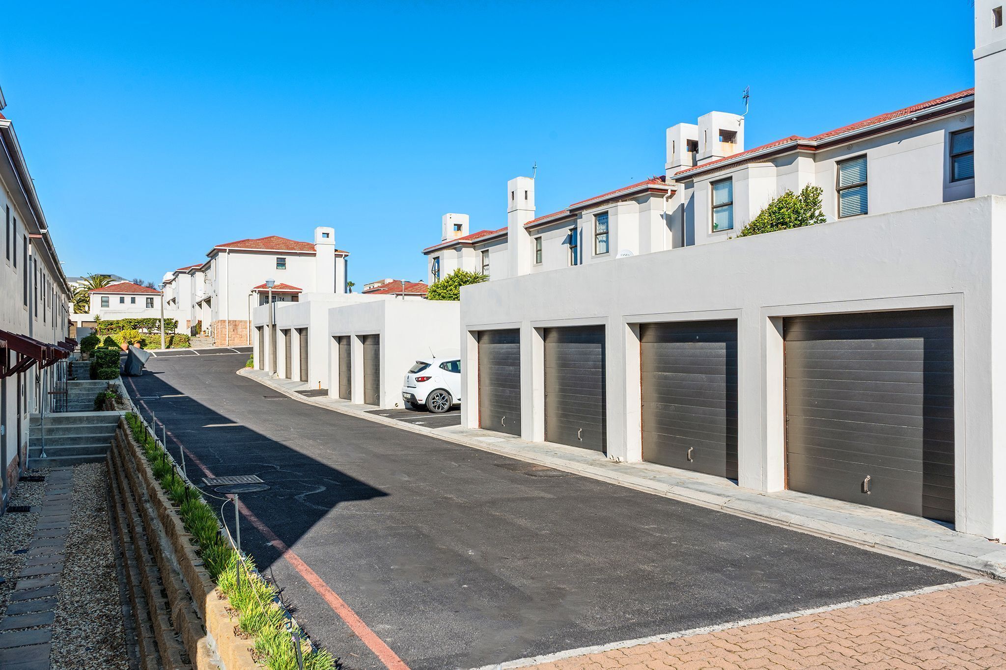 Une rue bordée d’immeubles modernes, une voiture blanche garée et un ciel bleu dégagé.