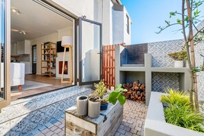 A modern house with a patio, a wooden bench, potted plants, and a visible kitchen area. - 42 Kronenbosch at West Beach (Cape Town)