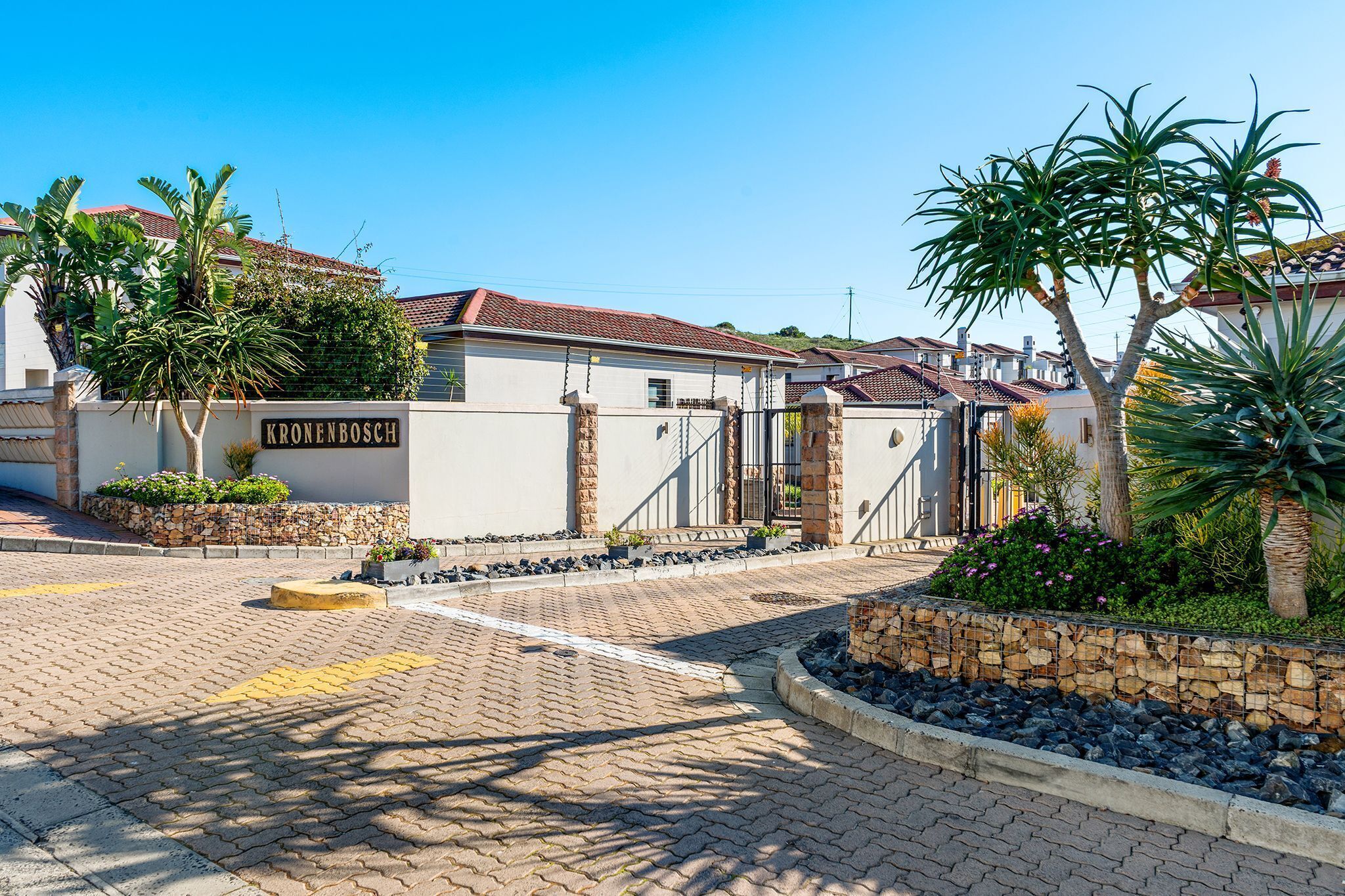 A gated residential area with a paved entrance, stone walls, and tropical plants.