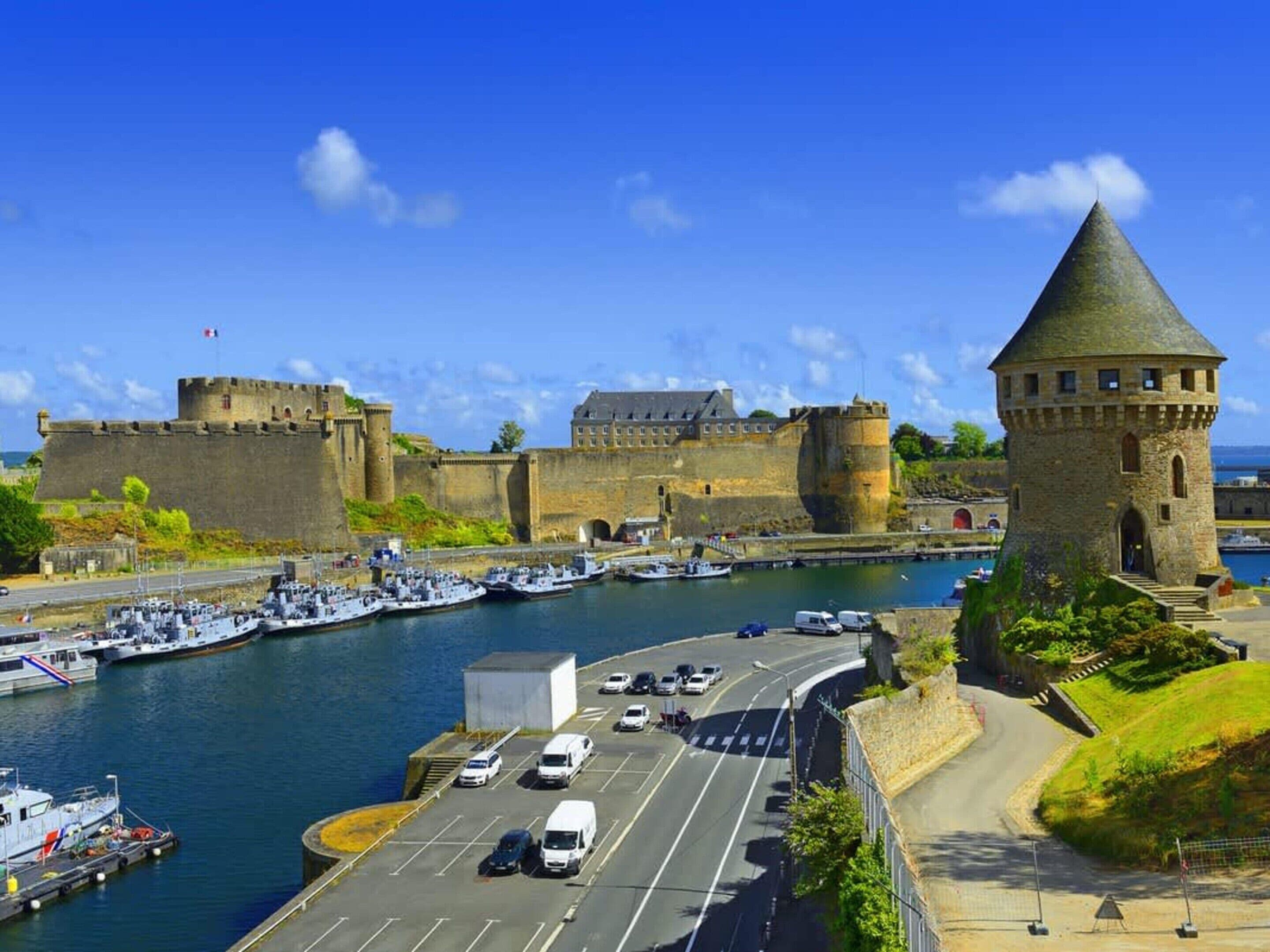 Une ville côtière qui abrite un château historique, une tour ronde et un port de plaisance rempli de bateaux.