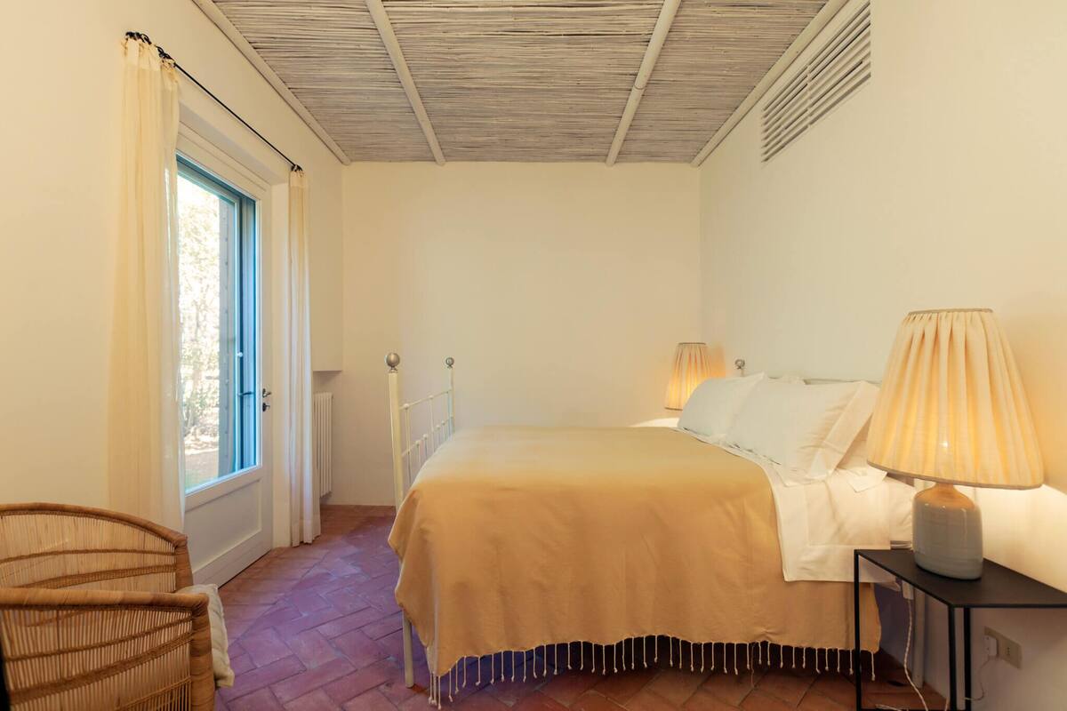 Une chambre à coucher avec un lit, des lampes de chevet, une chaise et une fenêtre avec des rideaux.