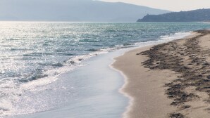 Uma praia com linha costeira curva, águas calmas e montanhas ao longe.