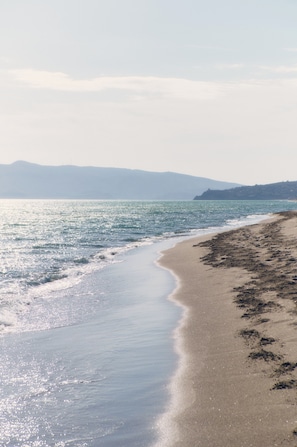 A beach with a curved shoreline, calm water, and distant mountains. - Terre di Sacra Ville & Cottage (Capalbio)