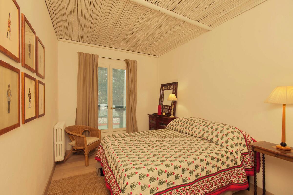 Une chambre à coucher avec un lit, une chaise, un radiateur, une fenêtre avec des rideaux et des tableaux encadrés accrochés au mur.