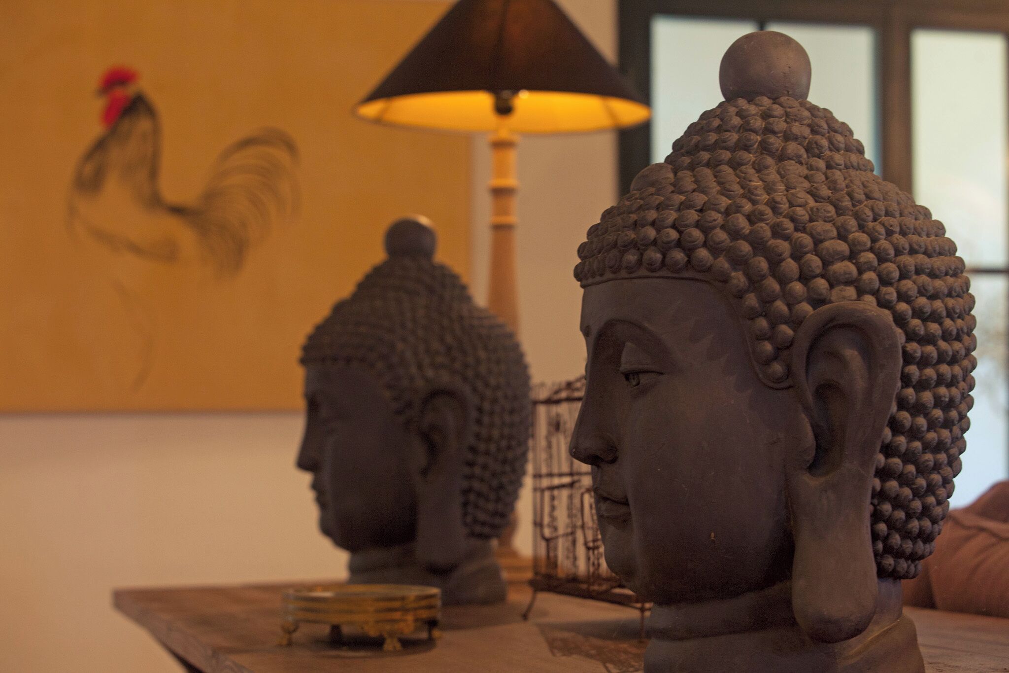 Una estatua de Buda, un cuadro de gallo y una lámpara en una habitación.