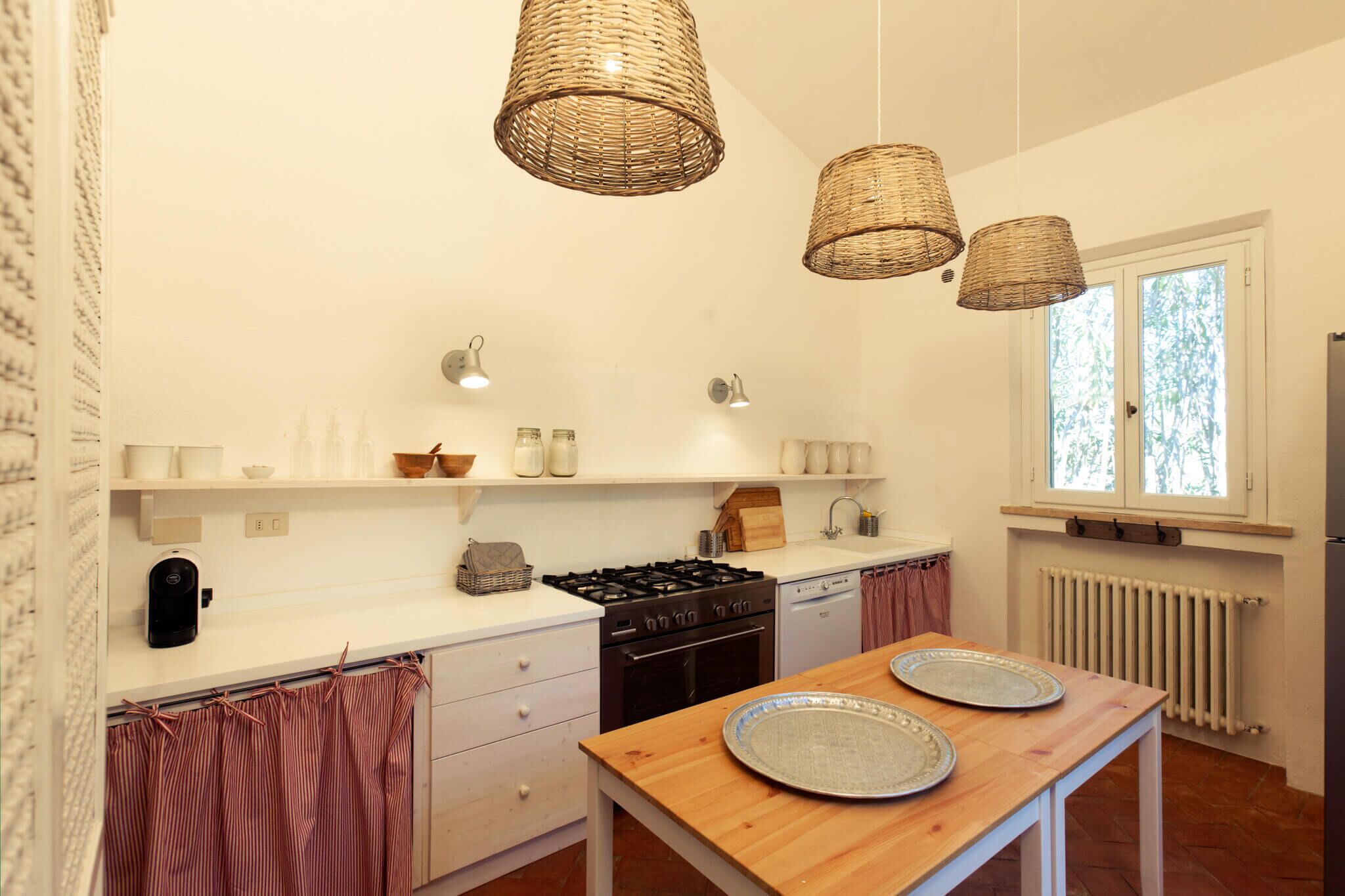 Una cocina moderna con armarios blancos, estufa a gas, lavavajillas y lámparas colgantes de mimbre.