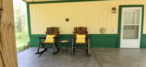 Two rocking chairs with yellow cushions on a porch with a green door and a small table. - Studio sleeps 4 with Full RV hookup & AC (Kalkaska)