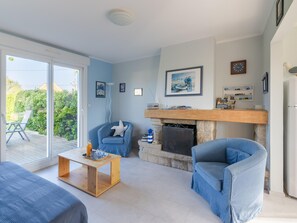 A living room with a fireplace, a blue armchair, a wooden coffee table, and a view of the outdoors. - Family Home Steps From the Beach (Ploudalmezeau)
