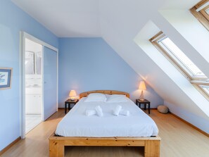 A bedroom with a wooden bed, two bedside lamps, a skylight, and a door leading to a bathroom. - Family Home Steps From the Beach (Ploudalmezeau)