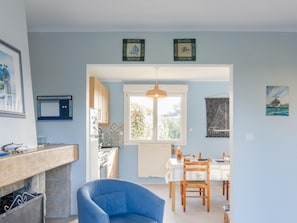 Ein Zimmer mit Esstisch, Stühlen, einem blauen Sessel, einem Kamin und einem Fenster.