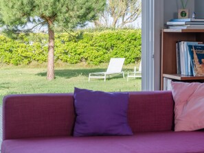 A purple sofa with a cushion, a white chair, and a bookshelf with books. - Family Home Steps From the Beach (Ploudalmezeau)