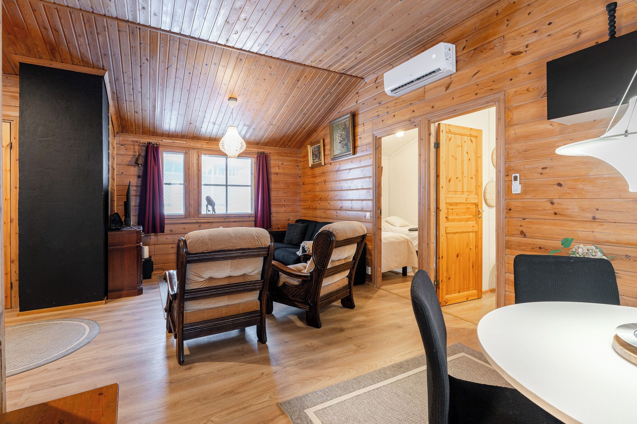Interior de una cabaña de madera con cama, sofá, mesa de comedor y ventilador de techo.