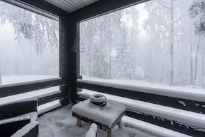 A snow-covered wooden bench outside a window with a view of a snowy forest. - Newly Renovated 2BR Cabin in Riihivuori (Muurame)
