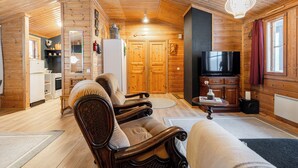 Un interior de madera con un sofá, sillas, un televisor y una zona de cocina.