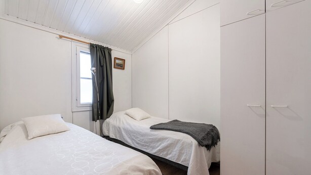 A bedroom with two beds, a wardrobe, a window with curtains, and a small picture on the wall. - Newly Renovated 2BR Cabin in Riihivuori (Muurame)