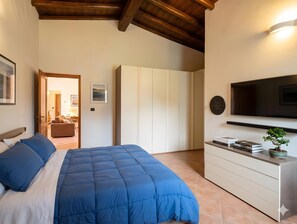 A bedroom with a bed, a TV, a dresser, and a door leading to another room.