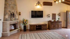 A living room with a stone fireplace, a flat-screen TV, wooden cabinets, and a stone wall. - Velletri, elegant guesthouse with pool (Greta's Villa) (Velletri)