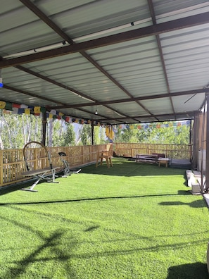 A covered outdoor area with artificial grass, exercise equipment, and a wooden fence.