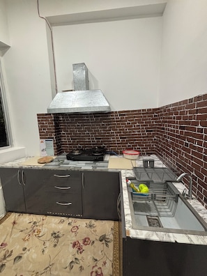 A compact kitchen with a gas stove, a sink, and a stainless steel range hood.