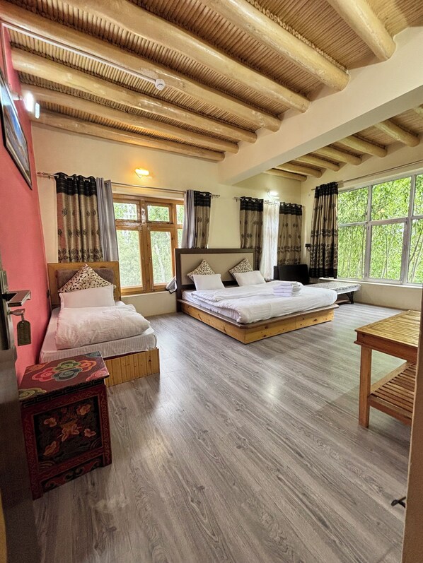 A bedroom with two beds, a wooden floor, a window, and a small table.