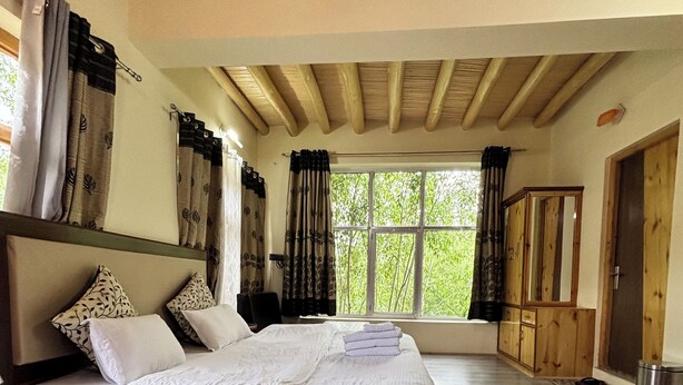 Een slaapkamer met een houten bed, grote ramen en uitzicht op groen.